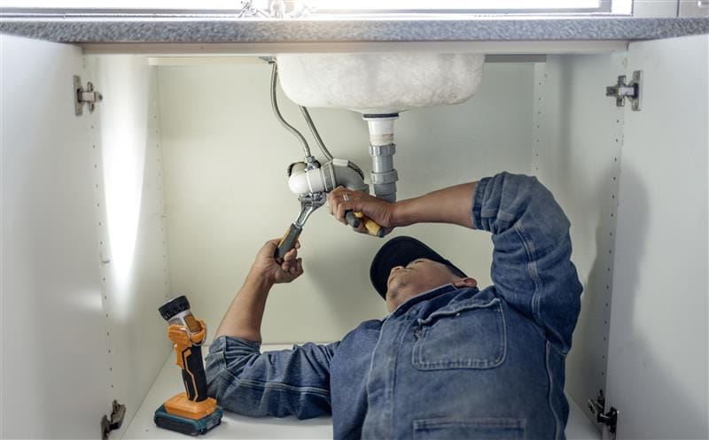 Plumber repairing pipes beneath a bathroom sink in Temecula