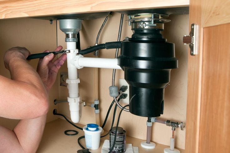 Plumber installing a garbage disposal beneath a kitchen sink in Temecula
