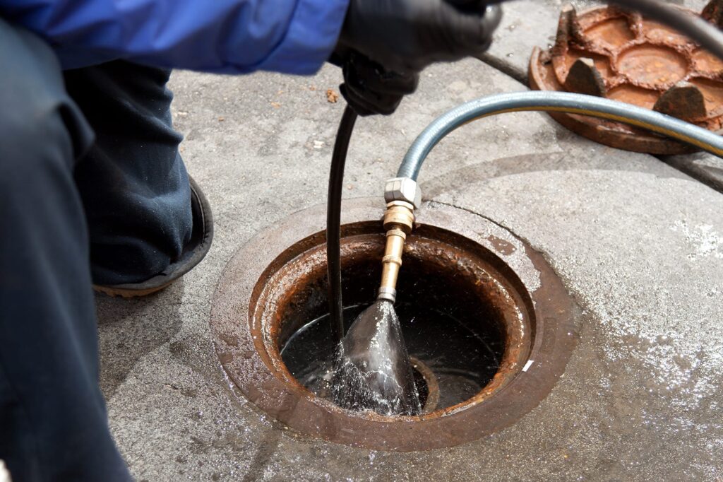 Plumber hydro jetting a sewer line through a manhole in Temecula