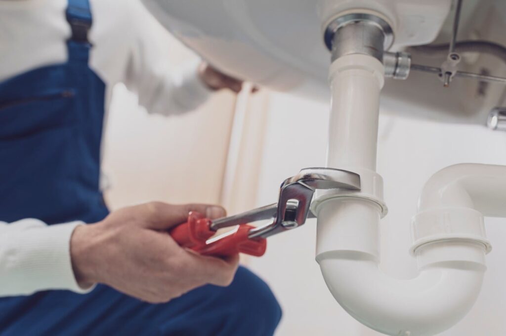 Plumber repairing a white drain pipe beneath a sink in Temecula