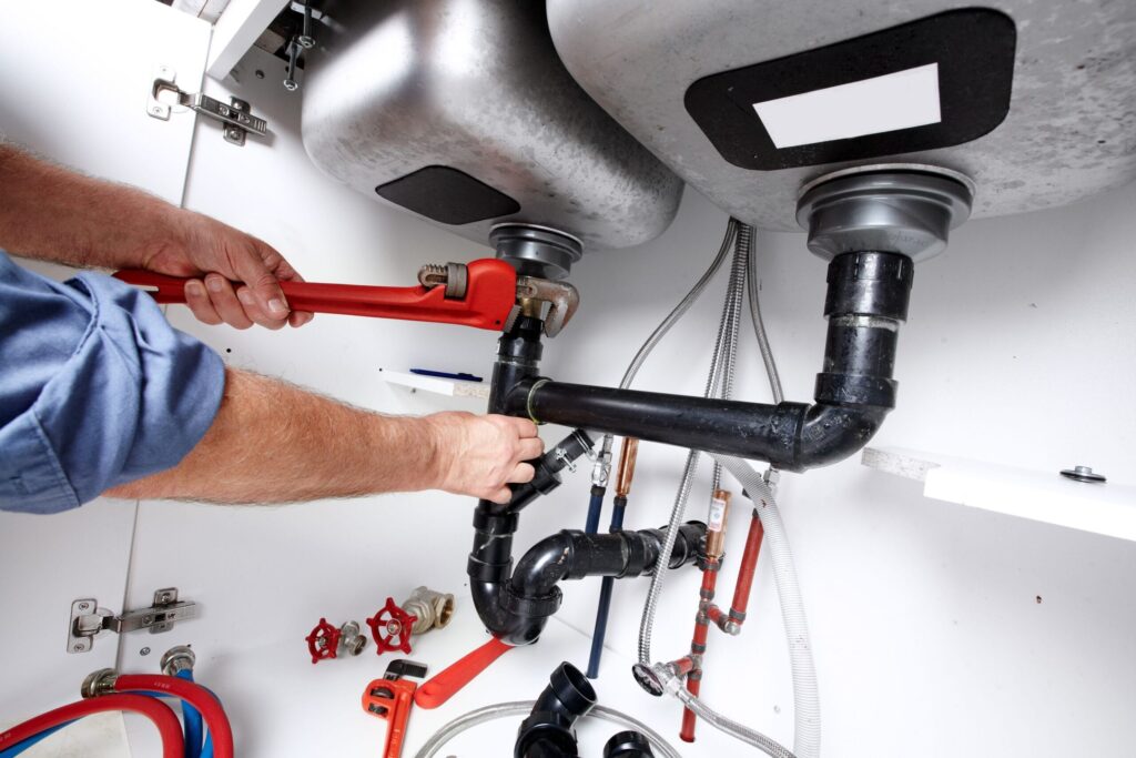 Plumber repairing drain pipes beneath a kitchen sink in Temecula